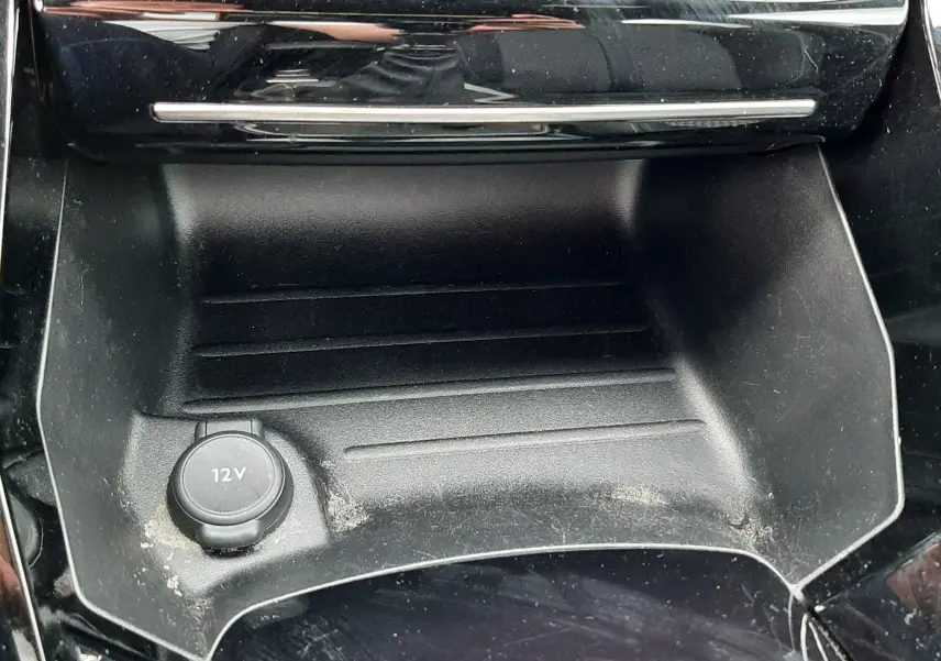Gros plan sur la prise 12V et le rangement noir brillant de la console centrale d'une Peugeot 208 gris Artense.