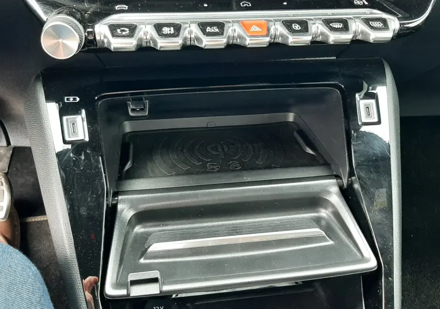 Détail de la console centrale noire de la Peugeot 208 1.2 100CH GT 2025, avec boutons chromés et compartiment ouvert.