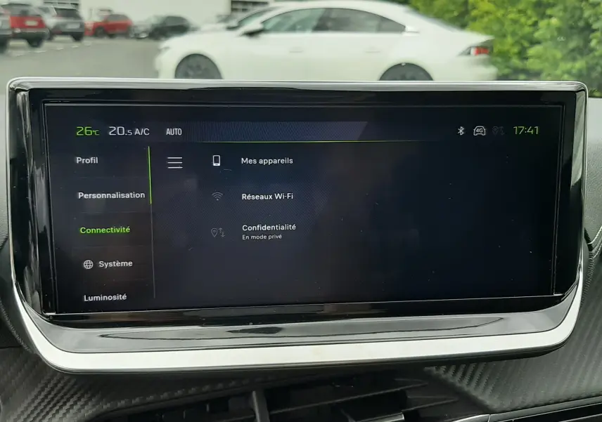 Écran tactile central du tableau de bord de la Peugeot 208 1.2 GT, affichant le menu connectivité, avec vue floue extérieure.