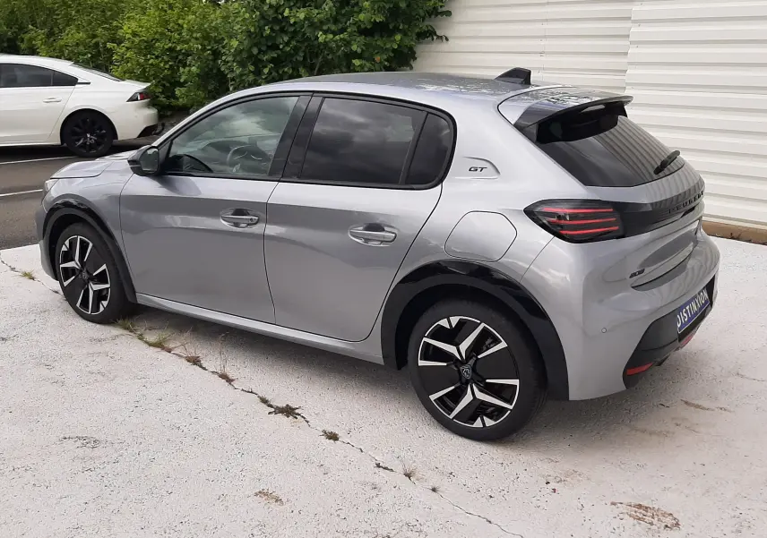 Peugeot 208 gris Artense vue 3/4 arrière côté gauche, avec jantes noires et logo GT sur l'aile arrière.