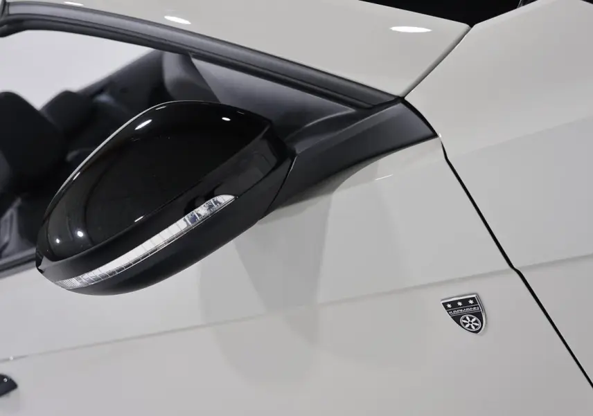 Gros plan sur le rétroviseur noir et l’écusson Karmann du côté gauche d’un Volkswagen T-Roc Cabriolet beige métallisé.