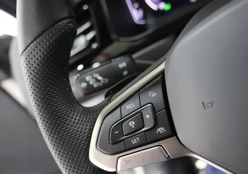 Gros plan sur les commandes de régulateur de vitesse au volant cuir perforé du Volkswagen T-Roc Cabriolet beige métallisé.