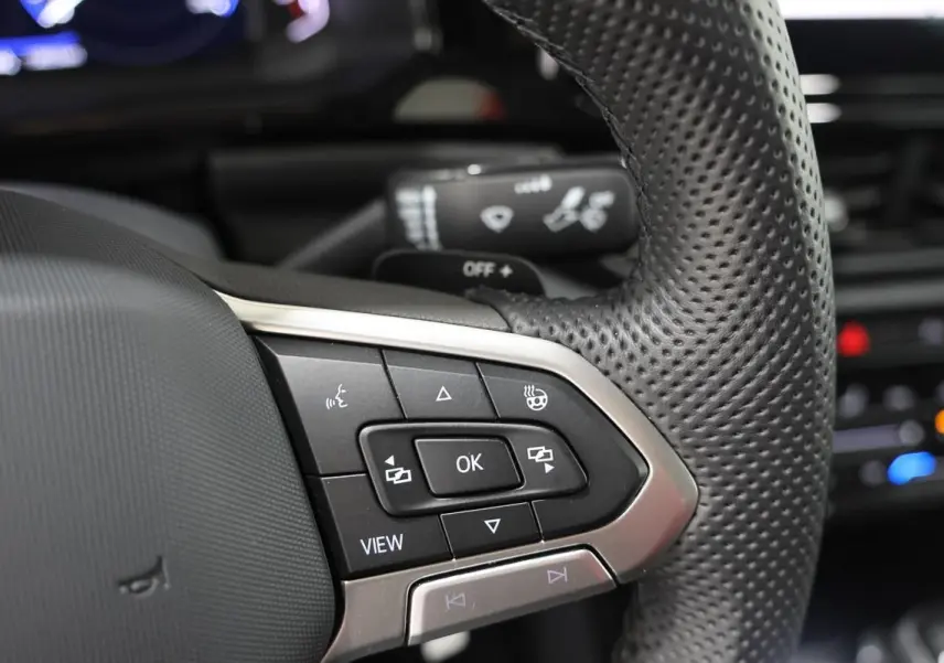 Gros plan sur les commandes multifonctions en cuir perforé du volant du Volkswagen T-Roc Cabriolet beige métallisé.