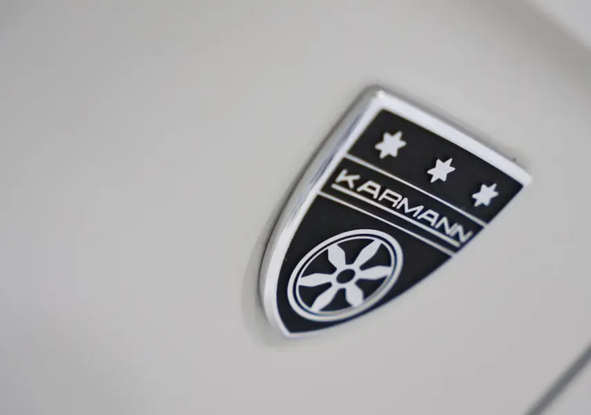 Gros plan sur l’écusson Karmann noir et argent sur la carrosserie beige métallisée du Volkswagen T-Roc Cabriolet.