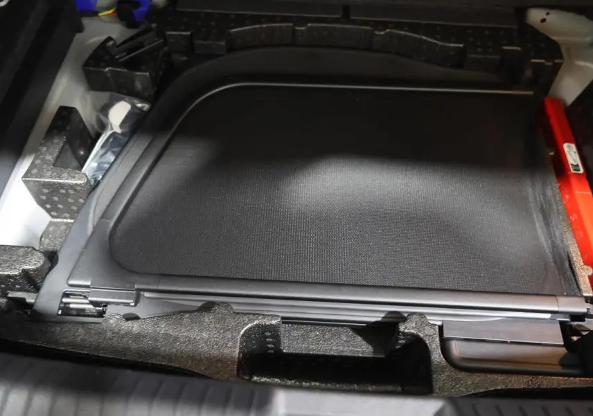 Rangement sous coffre montrant un filet de protection noir et des accessoires dans un Volkswagen T-Roc Cabriolet beige.