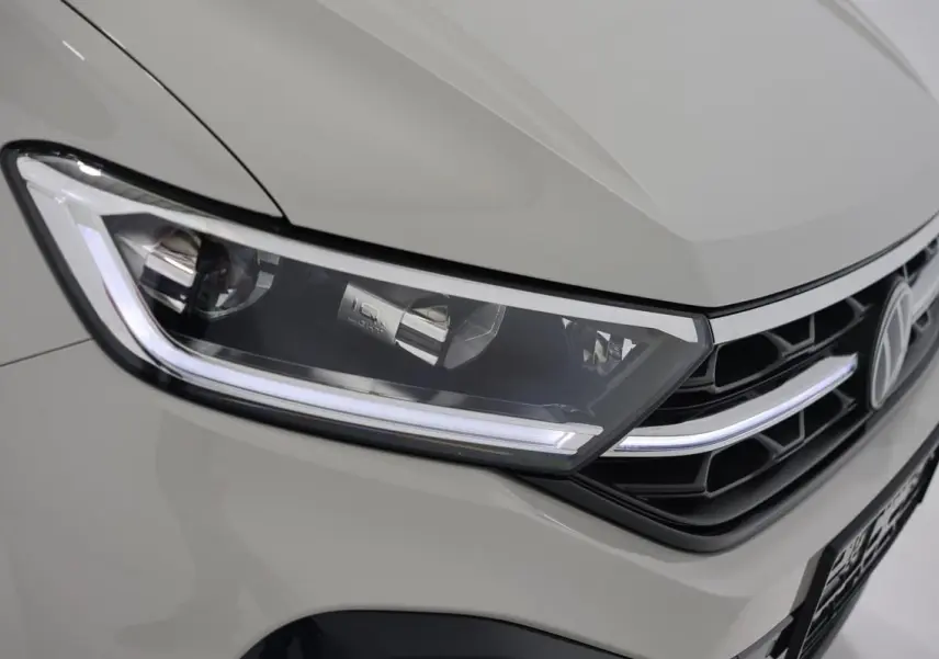 Gros plan sur le phare avant gauche et la calandre noire d’un Volkswagen T-Roc Cabriolet beige métallisé.