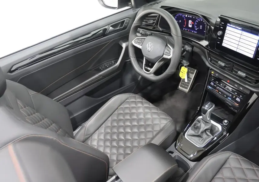 Vue intérieure côté conducteur du Volkswagen T-Roc Cabriolet 2025, sièges cuir noir matelassé avec surpiqûres orange.