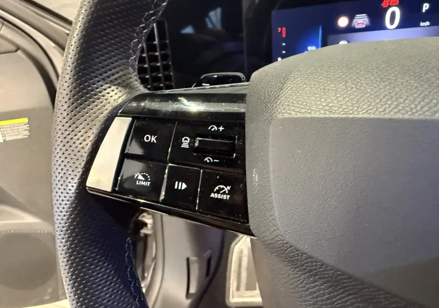 Gros plan sur les commandes du volant en cuir perforé de l’Opel Astra Sports Tourer gris, version 2024, côté gauche.