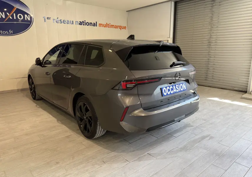 Vue 3/4 arrière droite d'une Opel Astra Sports Tourer gris métallisé avec jantes noires et vitres teintées.