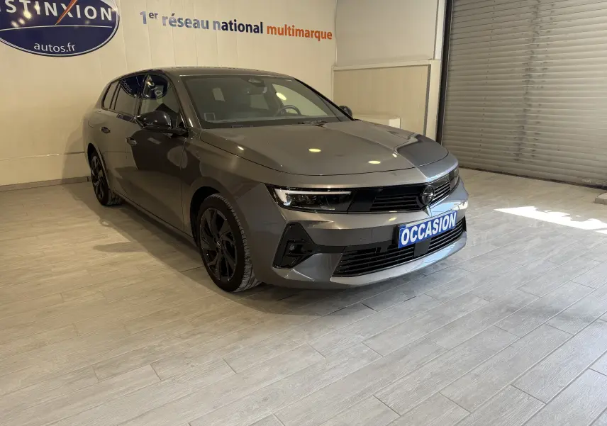 Vue 3/4 avant d'une Opel Astra Sports Tourer gris métallisé 2024 avec jantes noires et plaque "OCCASION".