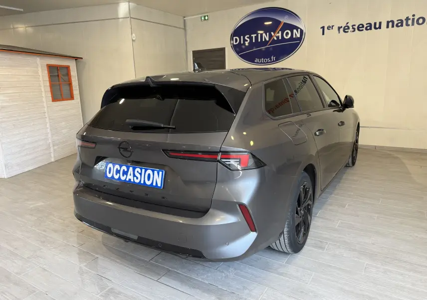 Opel Astra Sports Tourer gris vue 3/4 arrière droit en intérieur avec vitres teintées et jantes noires.