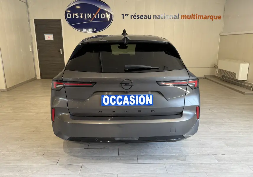 Vue arrière d'une Opel Astra Sports Tourer gris 2024 avec vitres teintées et plaque "OCCASION" en intérieur showroom.