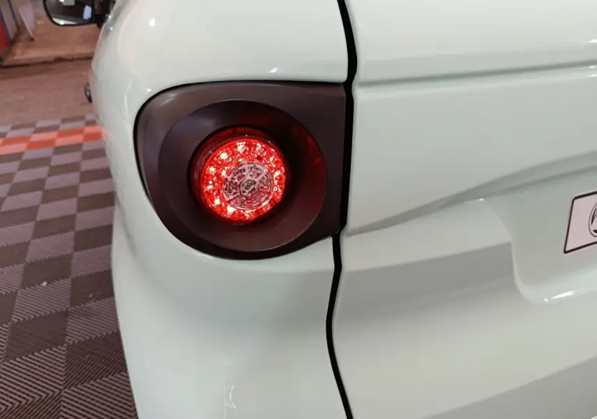 Gros plan sur le feu arrière gauche rouge d'une Aixam Ambition Easy Chic thermique verte, vue partielle arrière.