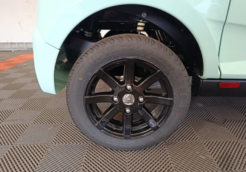 Gros plan sur la roue arrière droite noire de l'AIXAM AMBITION vert clair, avec logo central et suspension visible.