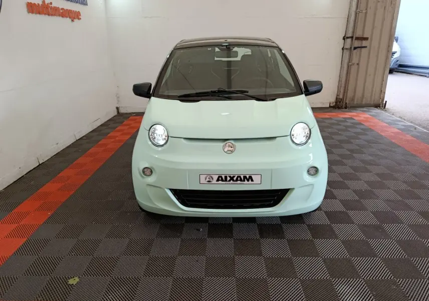 Vue frontale d'une Aixam Ambition Easy Chic thermique S10-2 2026 en vert clair avec toit noir dans un showroom.