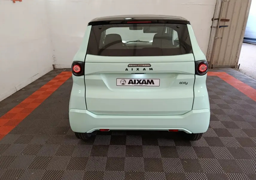 Vue arrière d'une Aixam Ambition Easy Chic 2026 vert clair avec feux ronds et toit noir dans un garage.