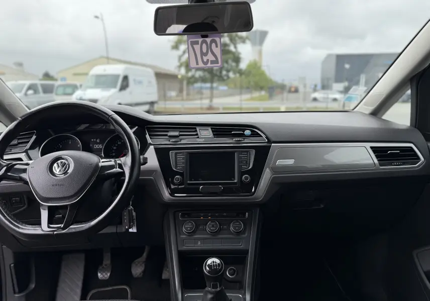 Vue intérieure frontale du Volkswagen Touran noir 2017, mettant en valeur le volant, la console centrale avec écran et la boîte manuelle.