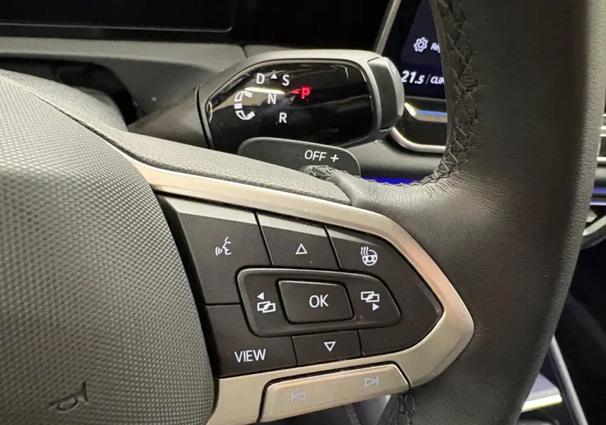 Gros plan sur les commandes au volant en cuir noir du Volkswagen Tiguan 2025, avec levier de vitesses automatique visible en arrière-plan.