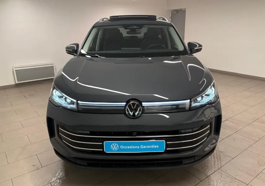 Vue de face du Volkswagen Tiguan 2.0 TDI 150 DSG7 Elegance en gris dauphin métallisé, avec phares allumés dans un intérieur neutre.