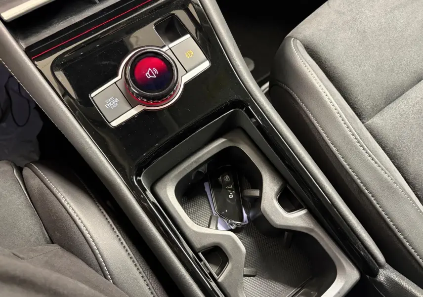 Gros plan sur la console centrale noire brillante du Volkswagen Tiguan 2025 avec bouton start/stop et porte-clés dans le porte-gobelets.