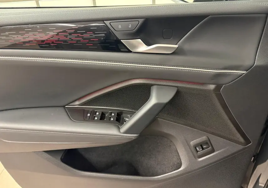 Vue intérieure côté gauche de la porte avant du Volkswagen Tiguan 2025, garniture noire avec surpiqûres blanches et bande décorative lumineuse.