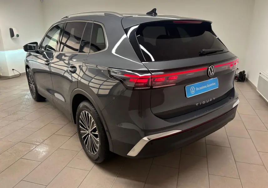 Vue 3/4 arrière droite d'un Volkswagen Tiguan gris dauphin métallisé, avec feux arrière allumés et jantes stylisées.