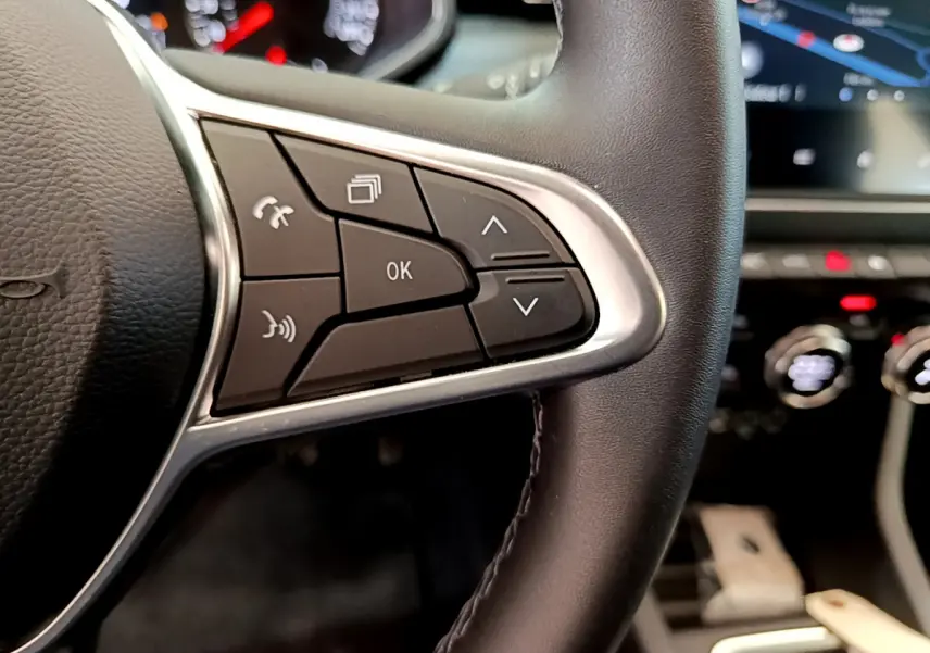 Gros plan sur les commandes gauche du volant cuir noir de la Renault Clio Business TCe 100, avec tableau de bord flou en arrière-plan.