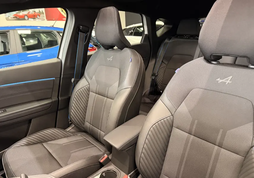 Vue intérieure des sièges avant gris foncé avec surpiqûres bleues et logo Alpine brodé sur les appuie-têtes.