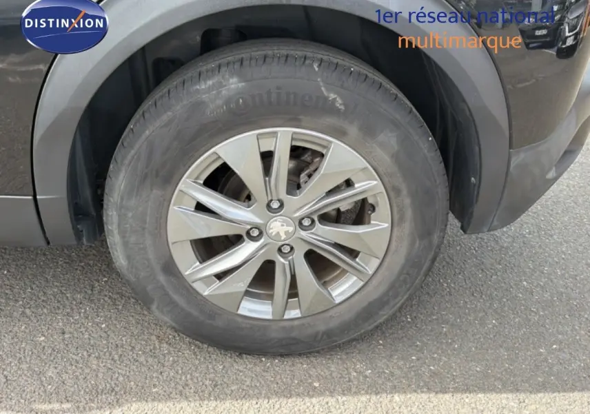 Gros plan sur la roue avant gauche d'un Peugeot 2008 noir perle métal, avec jante alliage et logo lion visible.