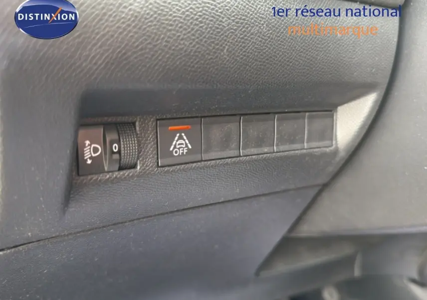 Gros plan sur les commandes de réglage des phares et de désactivation de l'alerte de franchissement de ligne dans un Peugeot 2008 noir perle 2022.