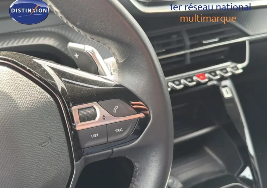 Gros plan sur le volant noir et les commandes multimédia d’un Peugeot 2008 2022, intérieur moderne avec tableau de bord noir brillant.