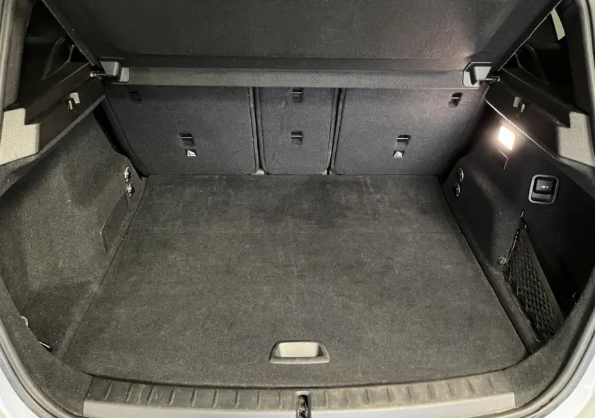 Coffre ouvert vu de face, intérieur noir avec éclairage latéral et filet de rangement sur la droite.