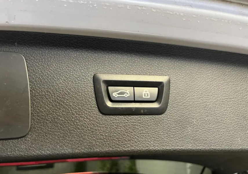 Boutons d'ouverture et de verrouillage du hayon sur la garniture intérieure d'un coffre de BMW Série 2 gris.