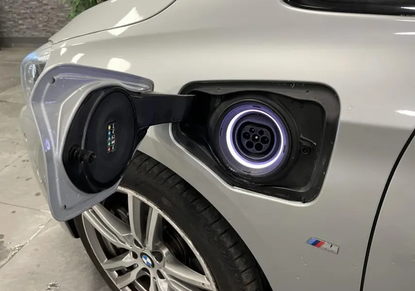 Prise de recharge ouverte côté gauche d’une BMW Série 2 225xe Active Tourer gris avec jante alliage et logo M visible.