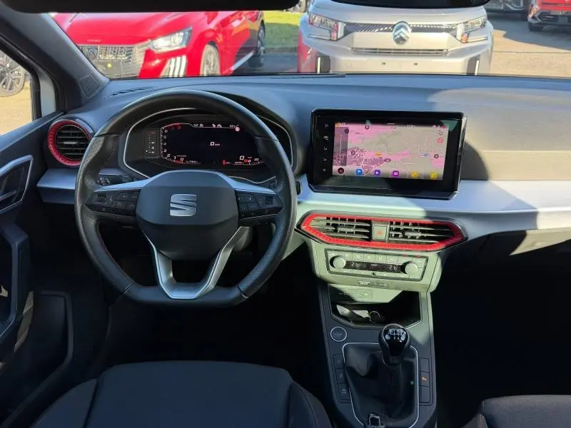 Vue intérieure avant de la SEAT Ibiza 1.0 TSI FR 2025, tableau de bord avec écran tactile et détails rouges autour des aérateurs.