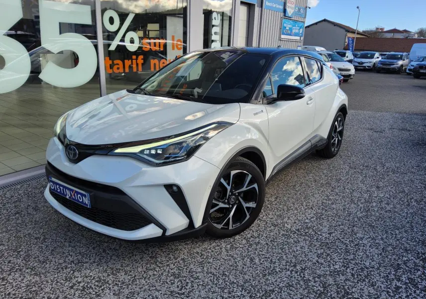 Toyota C-HR blanc nacré en 3/4 avant droit, avec jantes alliage noires et toit noir brillant visible.