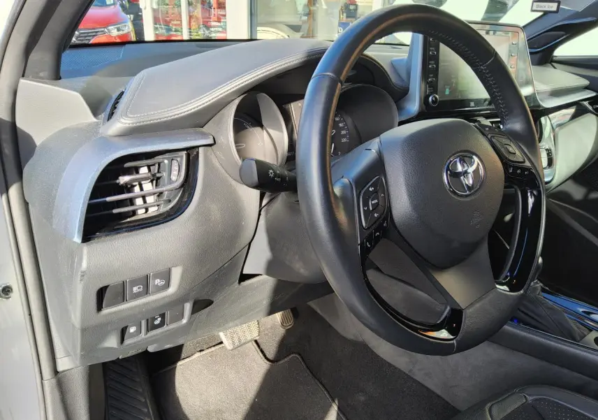 Vue intérieure côté conducteur du Toyota C-HR blanc nacré 2020, volant cuir multifonction et tableau de bord moderne.