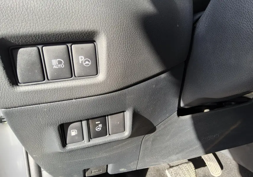 Gros plan sur les commandes côté conducteur du Toyota C-HR blanc nacré, avec boutons d'assistance et réglages divers.