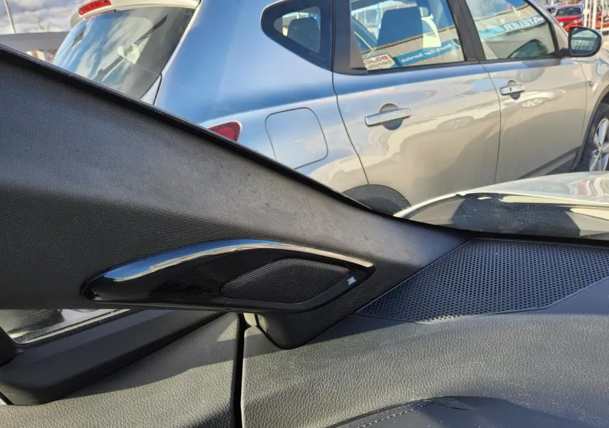 Vue intérieure côté droit sur l'enceinte JBL et la portière, avec une Toyota C-HR blanc nacré visible à l'extérieur.