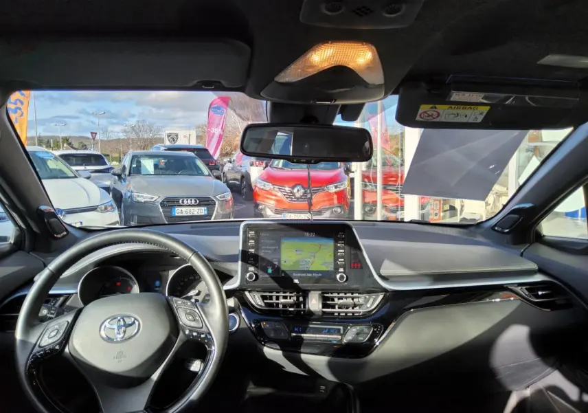 Vue intérieure avant du Toyota C-HR blanc nacré 2020, avec tableau de bord moderne et écran tactile central allumé.