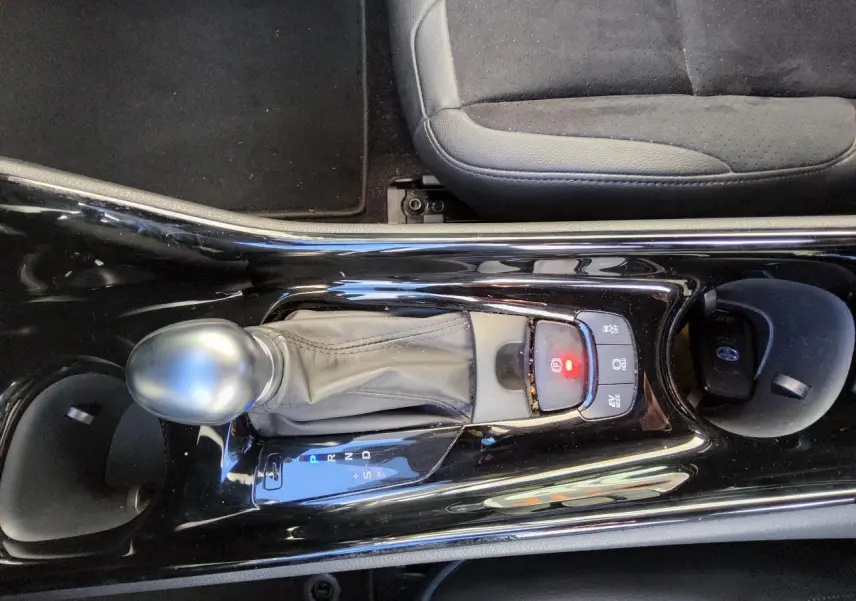 Vue rapprochée de la console centrale noire brillante avec levier de vitesse automatique et siège tissu gris du Toyota C-HR hybride.