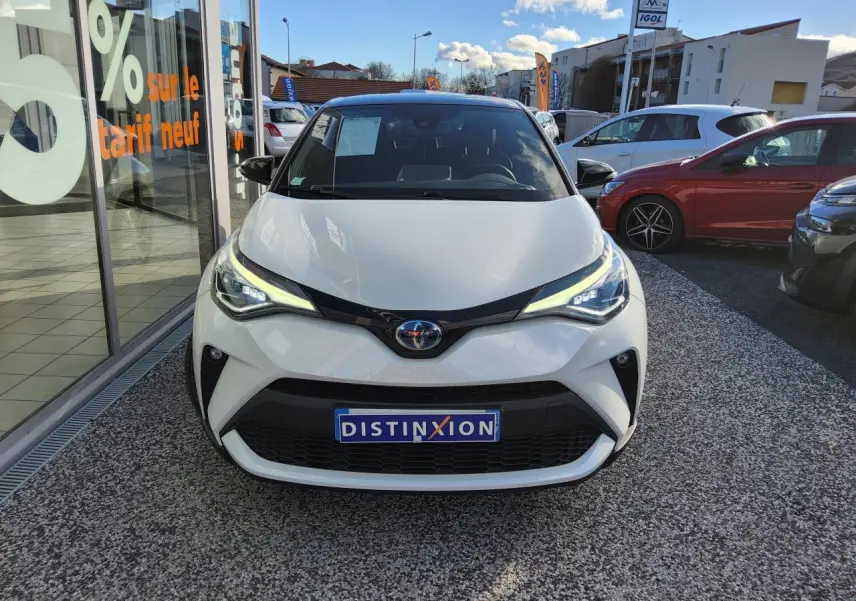 Vue avant d'une Toyota C-HR 2.0 Hybrid blanc nacré avec calandre noire et phares LED allumés.