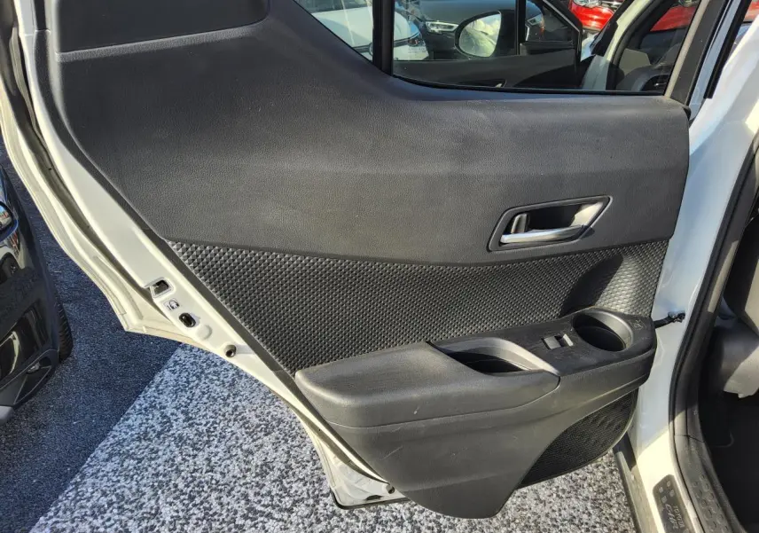 Vue intérieure de la porte arrière droite d’un Toyota C-HR blanc nacré, avec garniture noire texturée et poignée argentée.