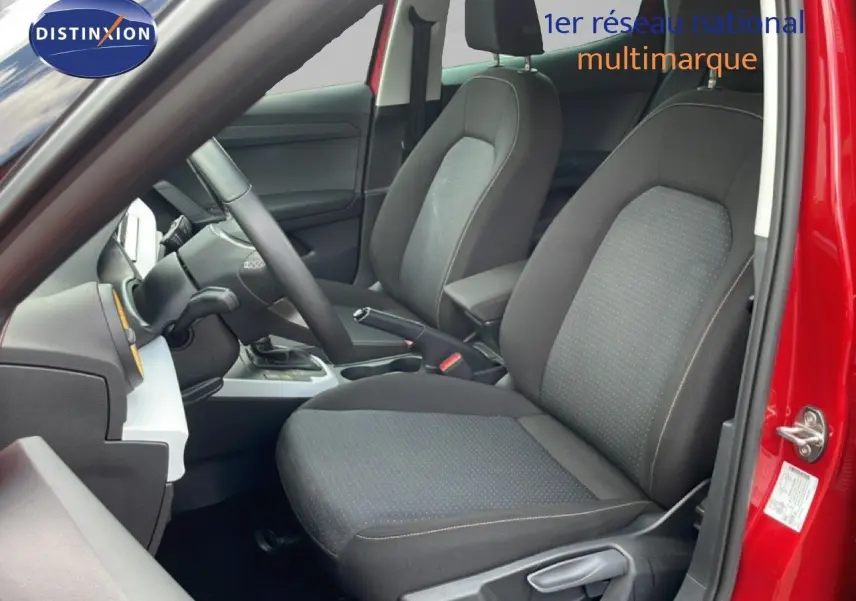 Vue intérieure côté conducteur du SEAT Arona rouge désir métal, mettant en valeur les sièges tissu noirs et le volant multifonction.
