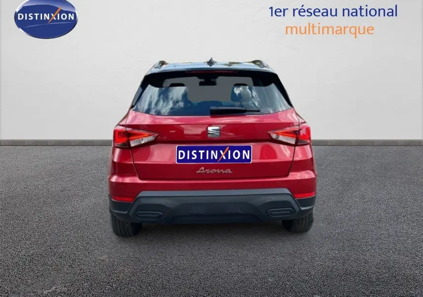 Vue arrière d'un SEAT Arona rouge Désir Métal avec toit noir, en stationnement devant un mur blanc.