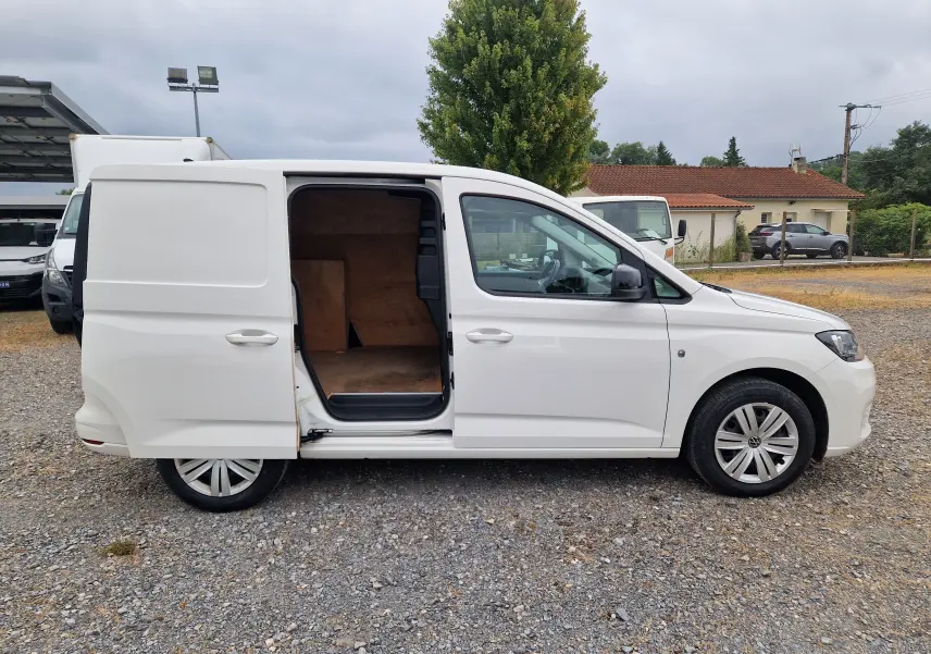 Vue de profil côté droit d’un Volkswagen Caddy Cargo blanc 2023 avec porte latérale coulissante ouverte montrant l’intérieur boisé.