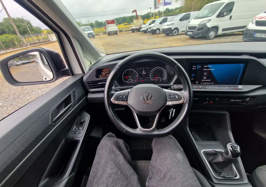 Vue intérieure depuis le siège conducteur du Volkswagen Caddy Cargo blanc 2023, volant multifonctions et boîte manuelle visibles.