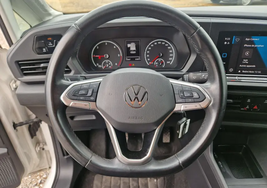 Vue intérieure centrée sur le volant noir du Volkswagen Caddy Cargo 2023, avec tableau de bord et écran tactile visibles.