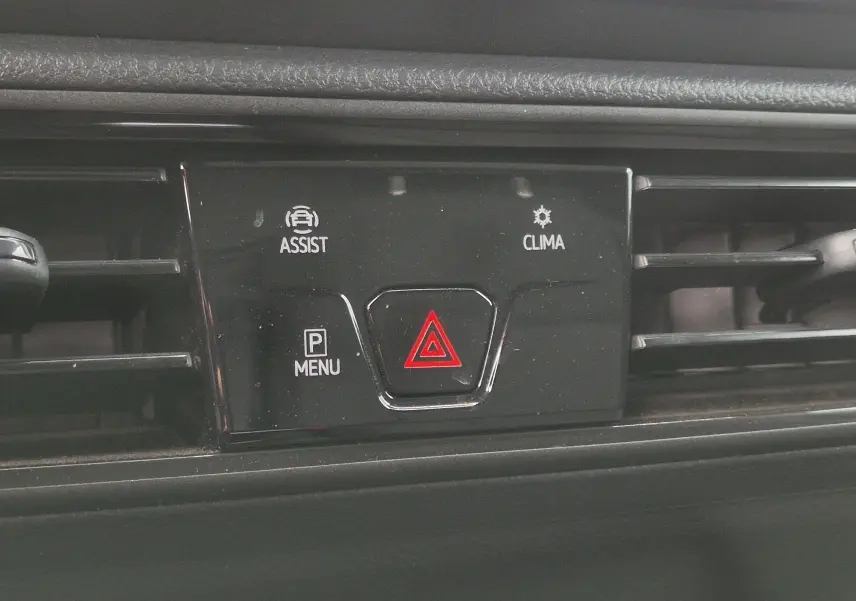 Gros plan sur la console centrale noire du Volkswagen Caddy blanc 2023, avec bouton de signalisation d’urgence rouge et commandes assist et clima.
