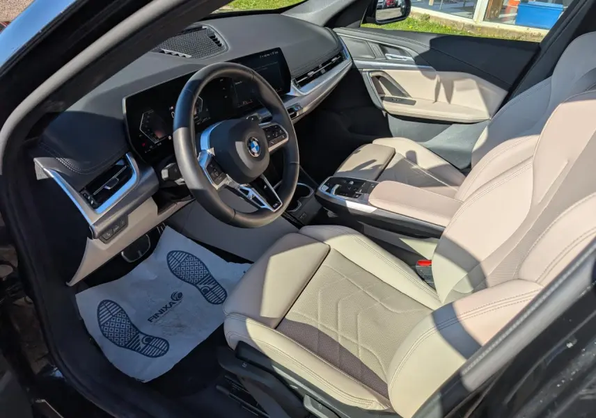 Vue intérieure côté conducteur du BMW X1 noir 2024, sellerie similicuir Oyster claire et tableau de bord moderne.